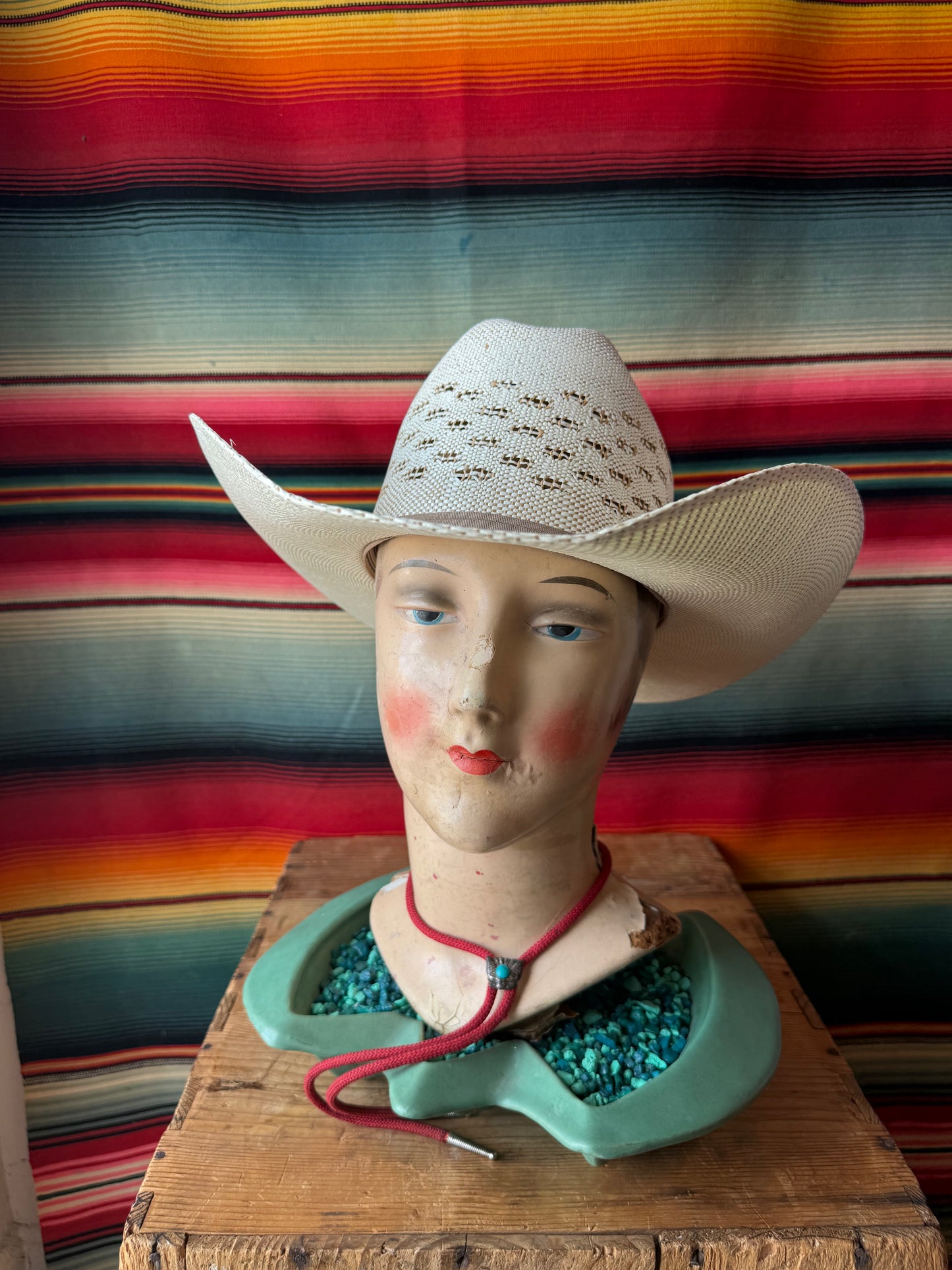 Mannequin head wearing a cowboy hat with a colorful striped fabric background