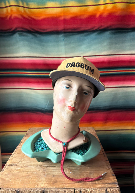 Mannequin head with a cap labeled 'DAGGUM' against a colorful striped background